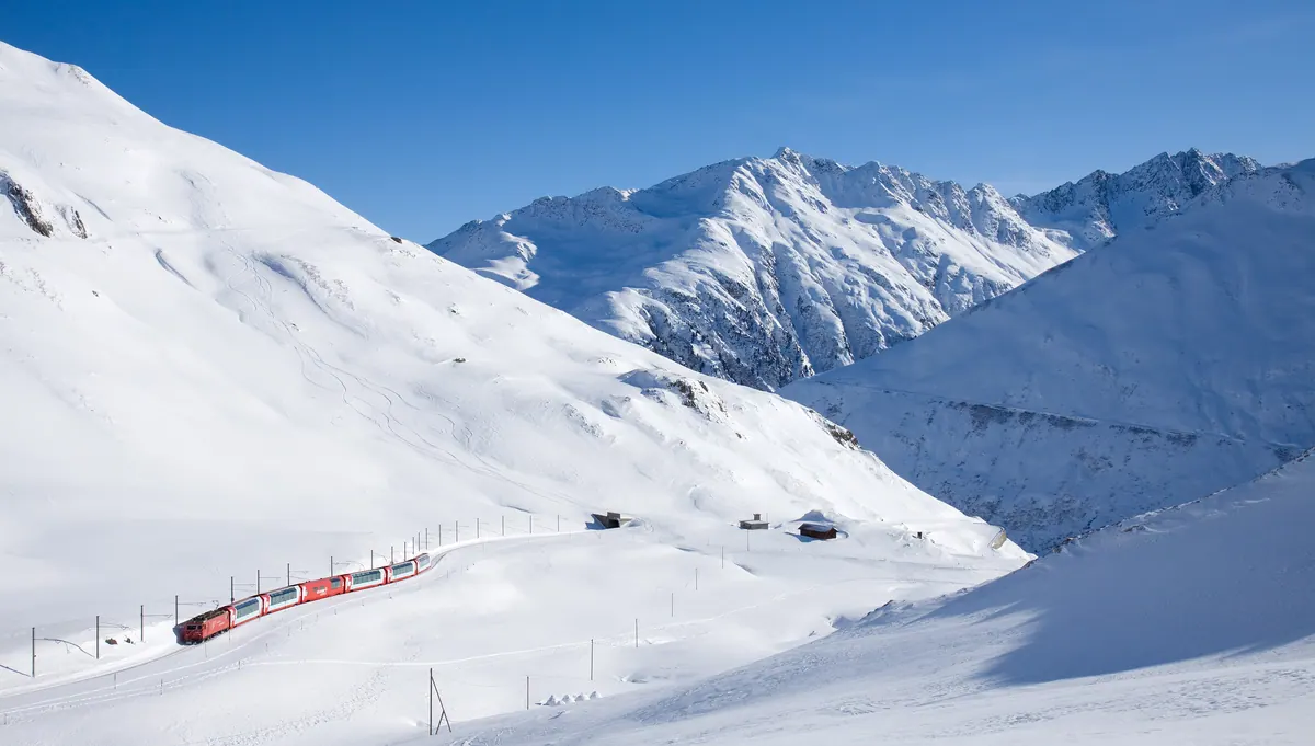 Glacier Express hauled by a red Matterhorn Gotthard Bahn locomotive just below the Oberalp Pass summit
