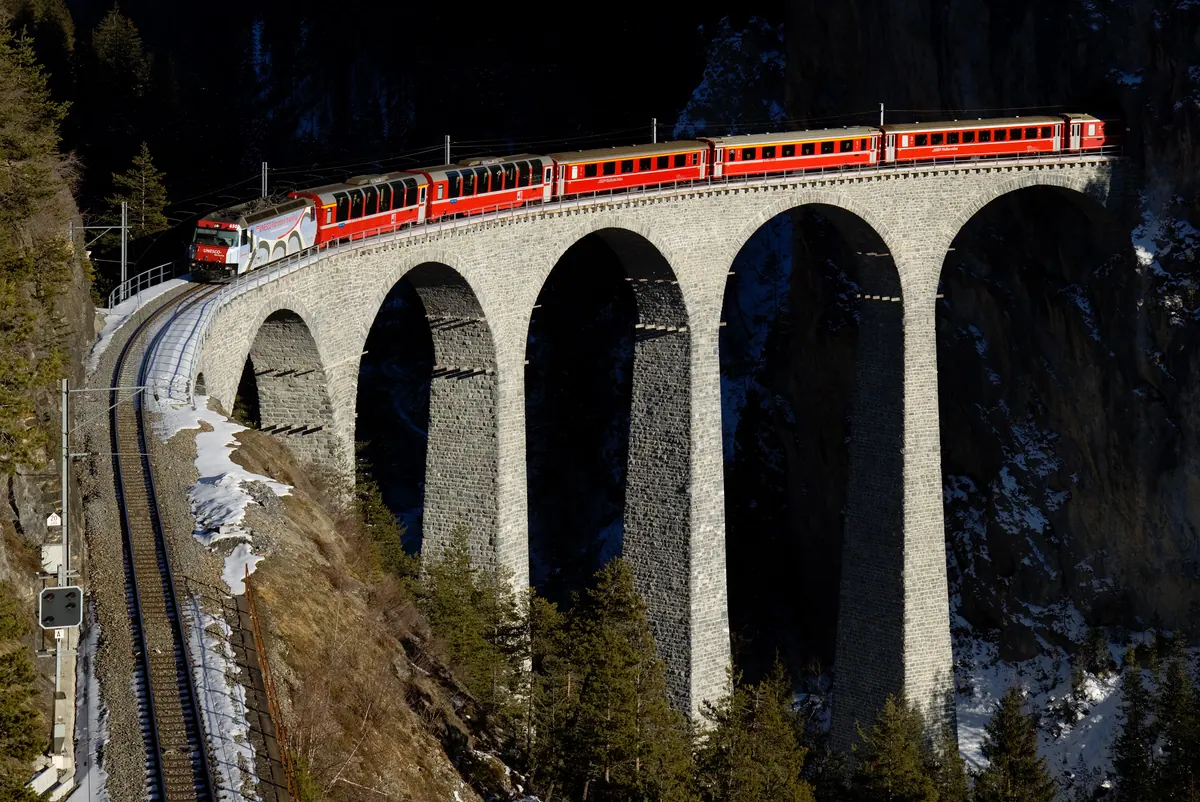 A red Rhaetian Railway train crossing the Landwasser Viaduct, part of the UNESCO-listed Albula line
